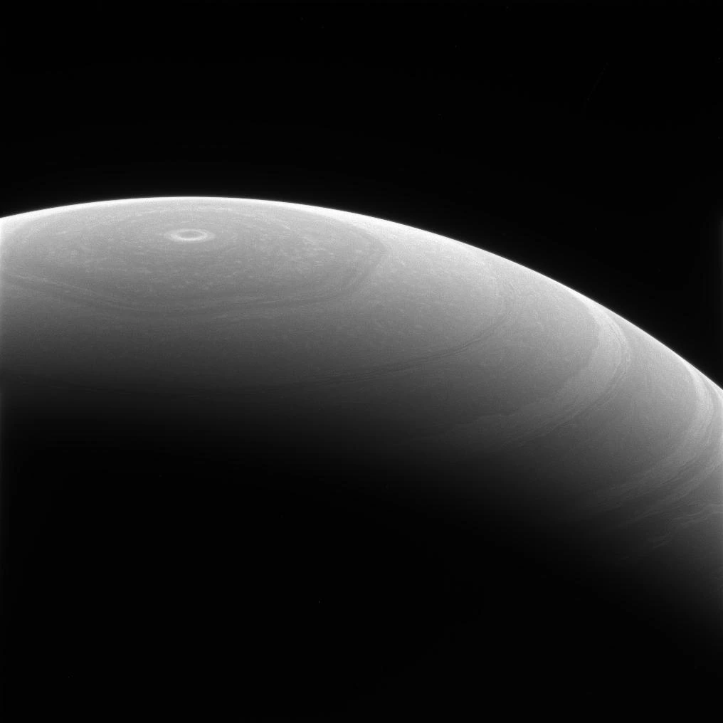 土星を斜め上から見た白黒の探査画像。丸い惑星の北極付近に、角のある雲の模様が見える